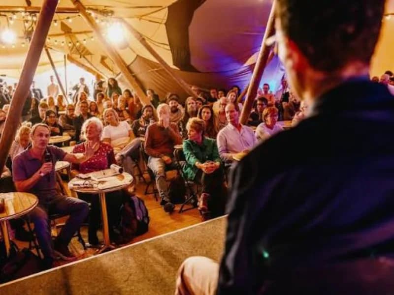 Audience inside a festival tent at a HowTheLightGetsIn talk, with an attendee asking a question.